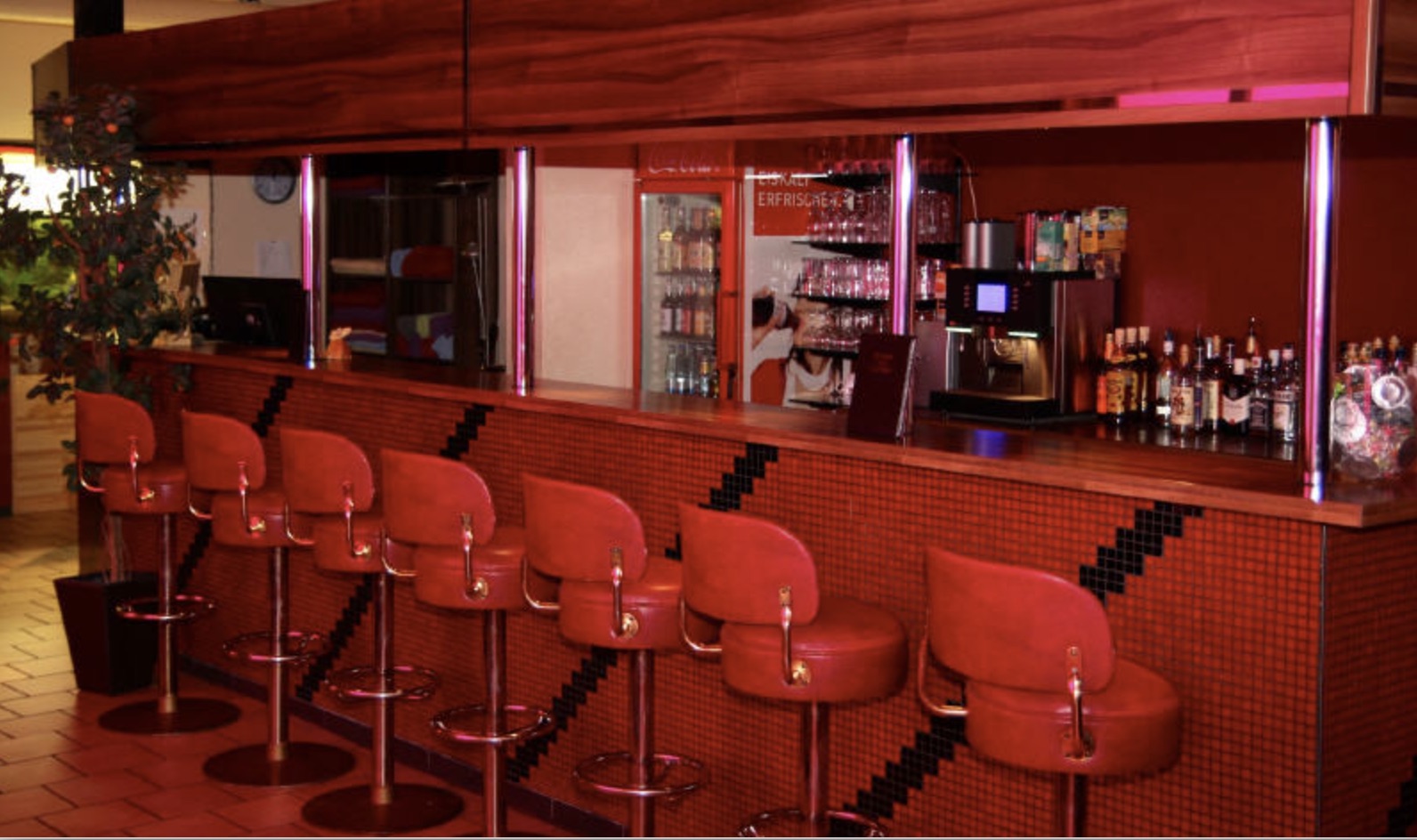 Bar mit roten Hockern, Mosaiktheke und Getränken.