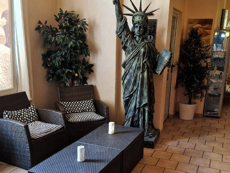 Sitzecke mit Freiheitsstatue, Rattansesseln und Pflanze.
