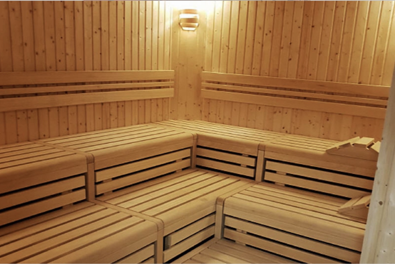 Helle Holzsauna mit Eckbänken und einer Lampe an der Wand.